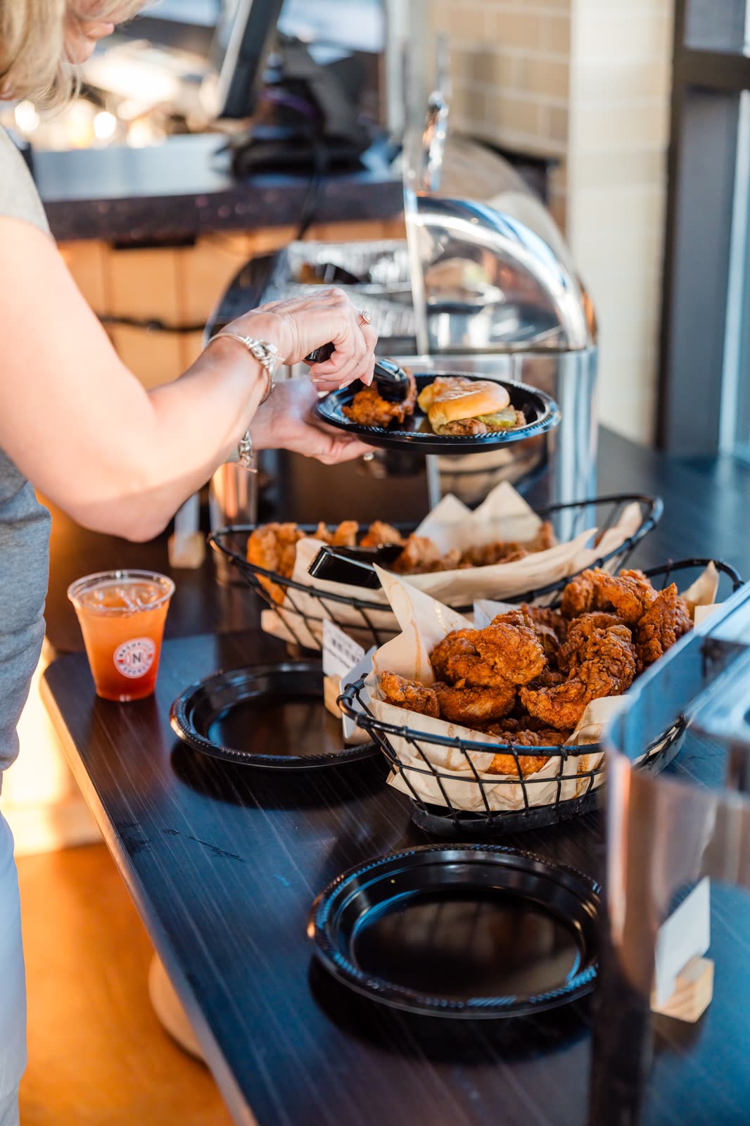 A guest plating hot chicken from baskets at a suite buffet