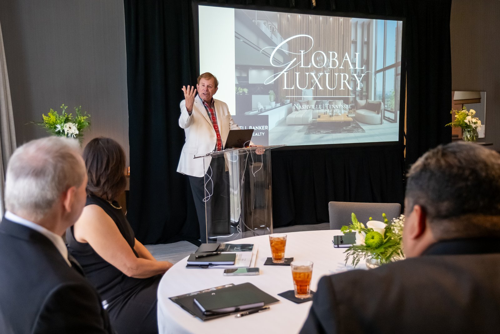 A speaker presenting from a lectern with his slide projected behind him