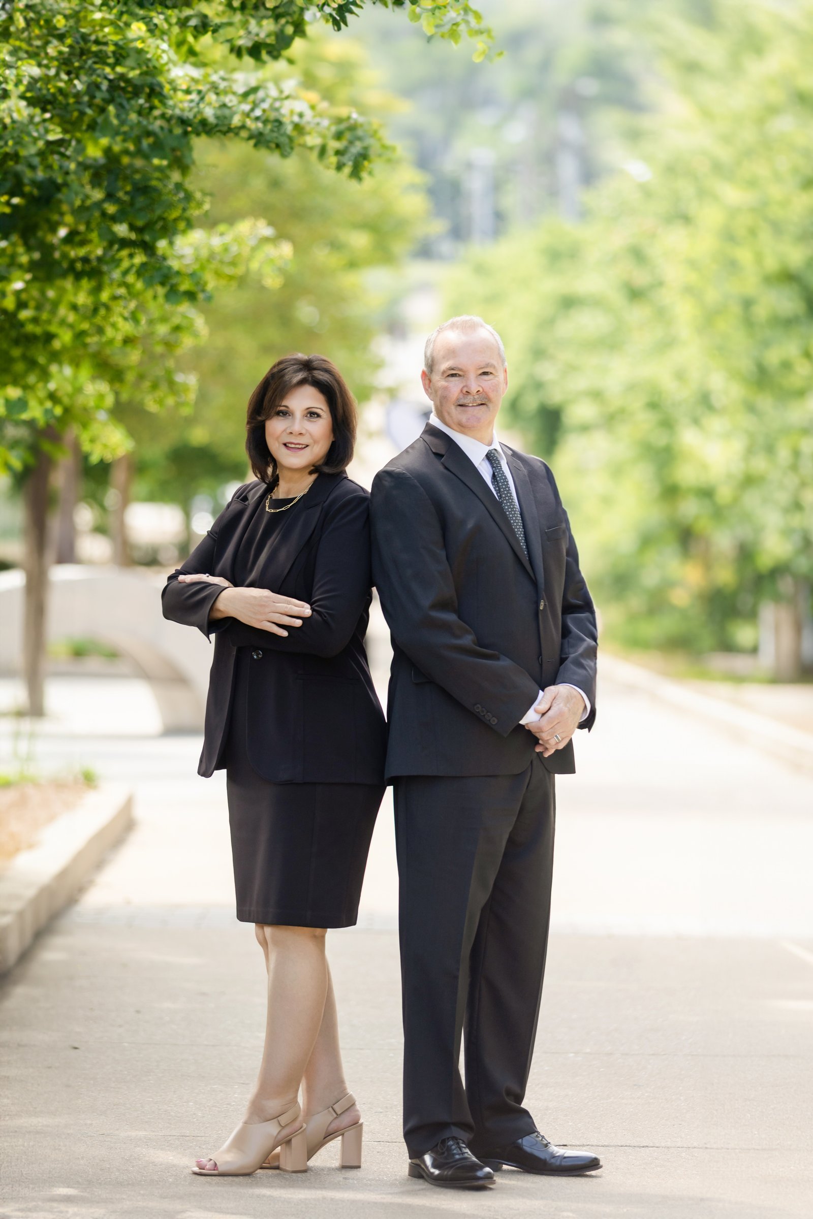 Two colleagues photographed back to back on a tree lined path