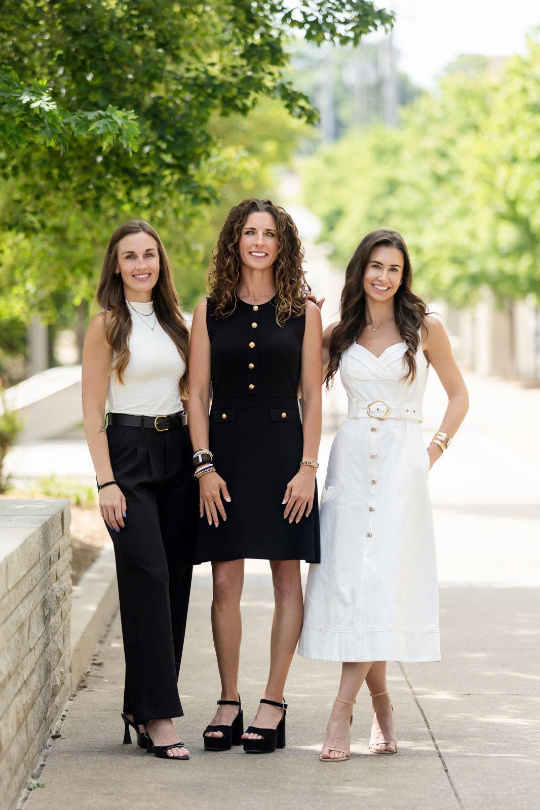 Three teammates in black and white posed together on a shaded sidewalk
