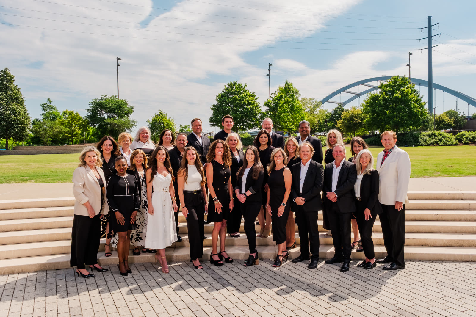 A team of nearly thirty in black and white outfits on riverfront steps, an arched bridge behind them