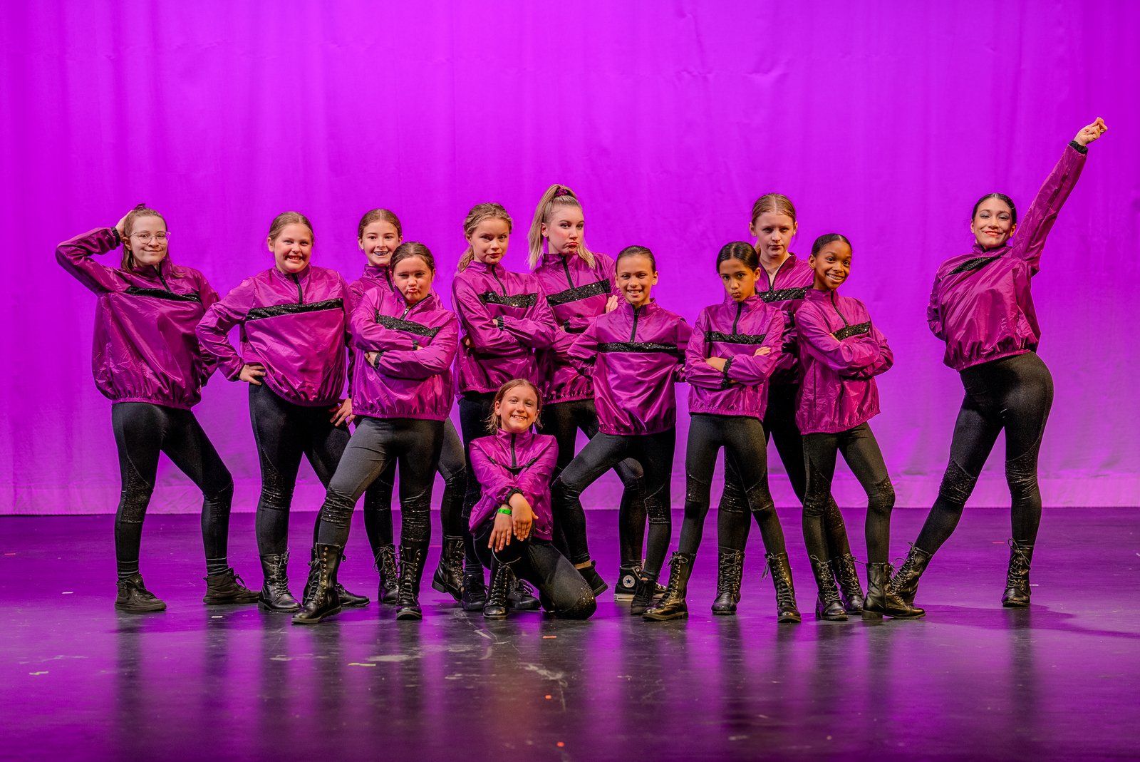 A hip hop group posed on stage in magenta jackets under purple light
