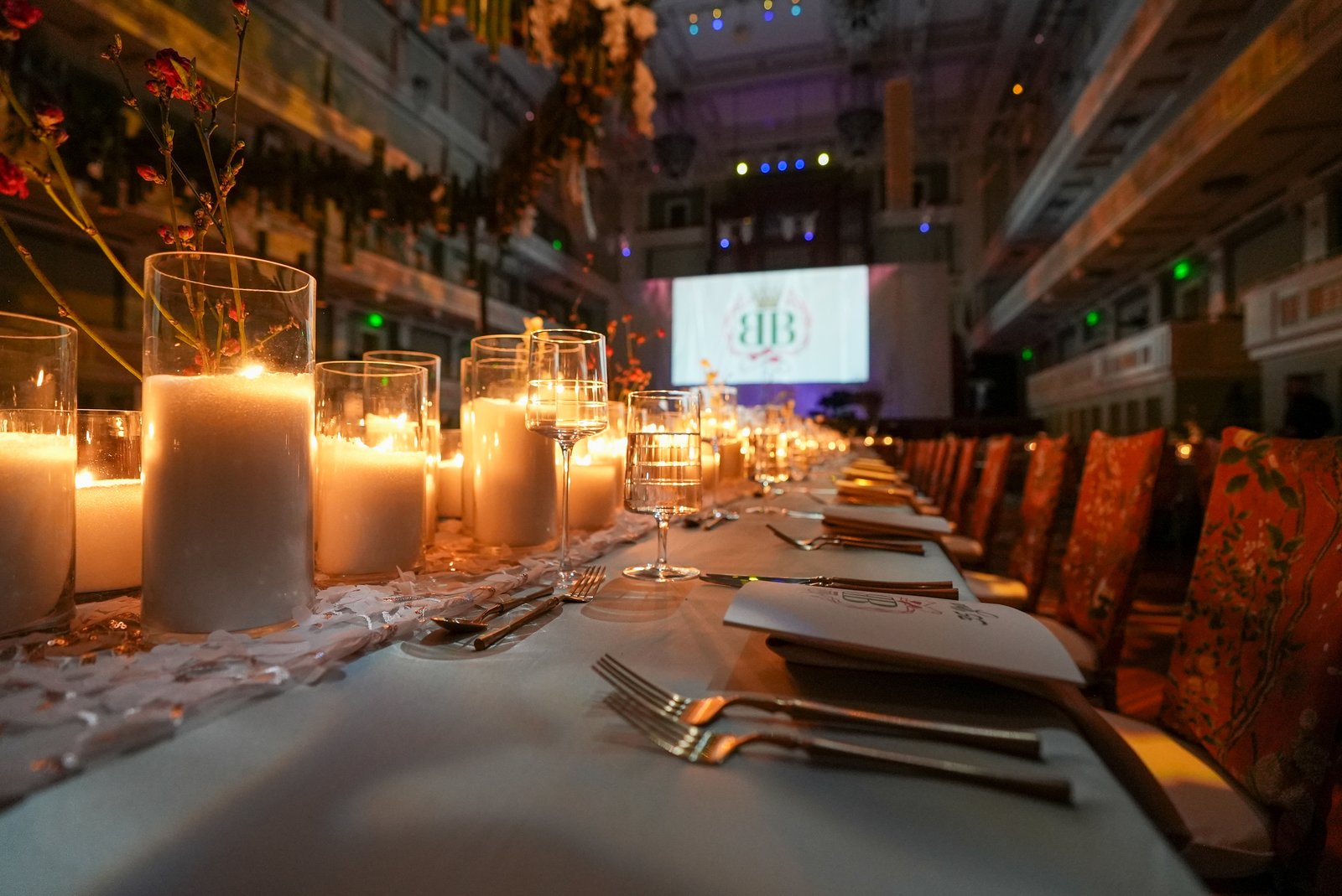 A long banquet table lit by candles running toward a lit stage