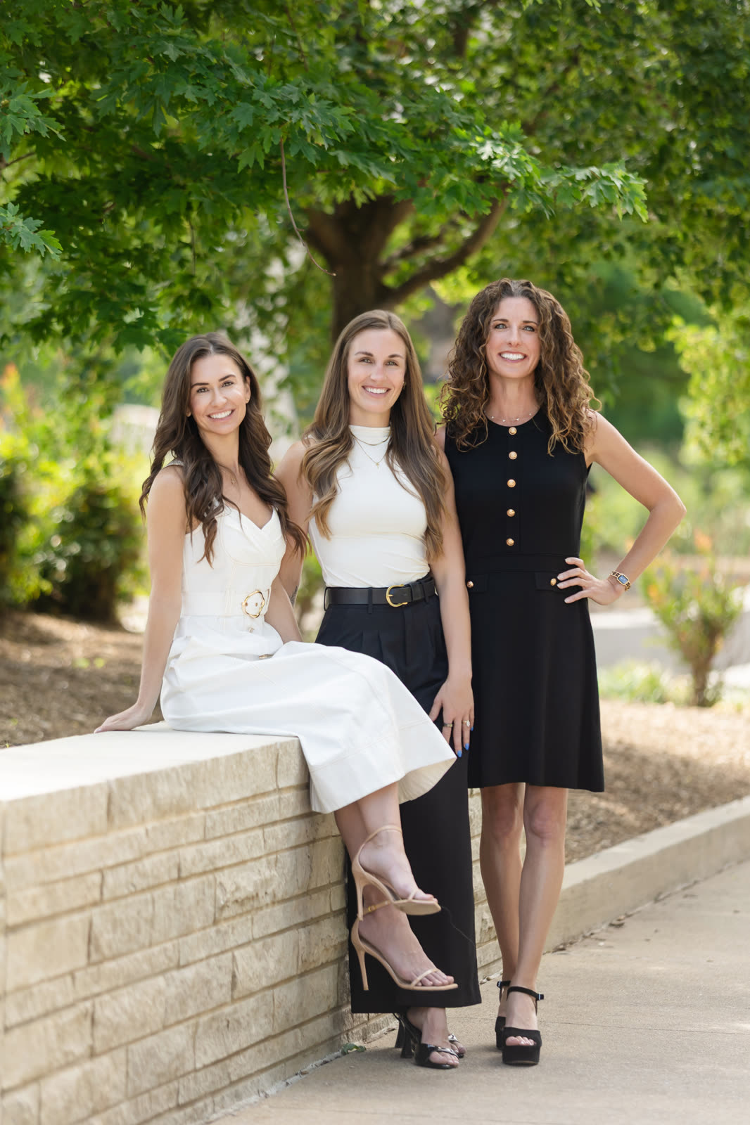 Three teammates in summer dresses, one seated on a stone wall