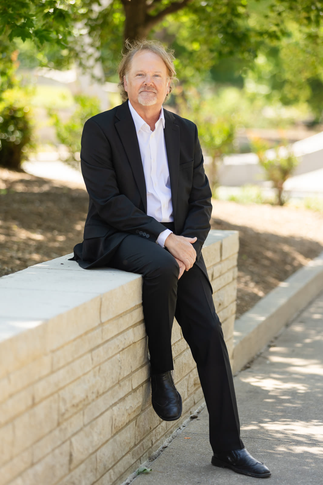 A team member in a suit seated on a low stone wall