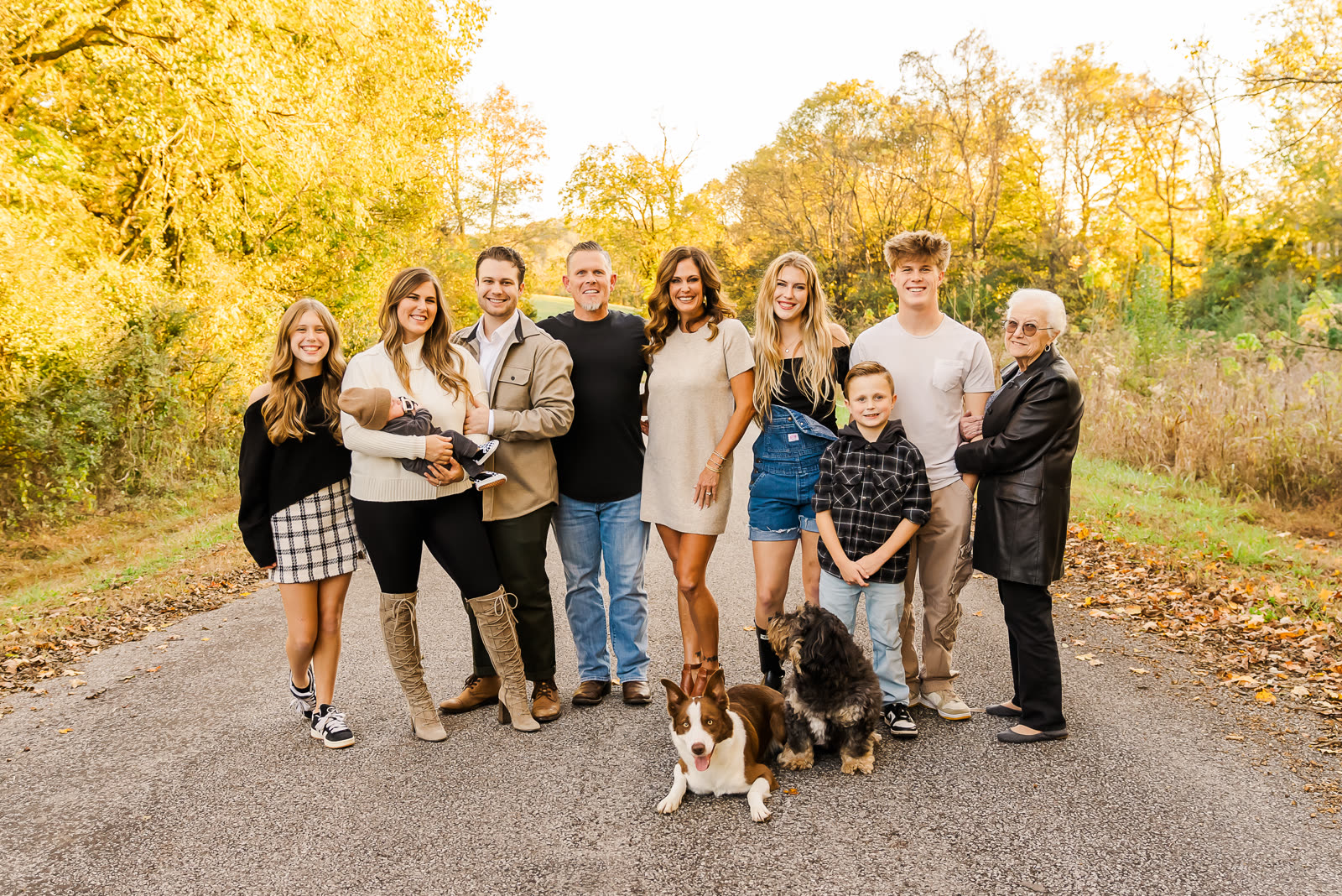 A three-generation family with two dogs gathered on a country road lined with golden fall trees