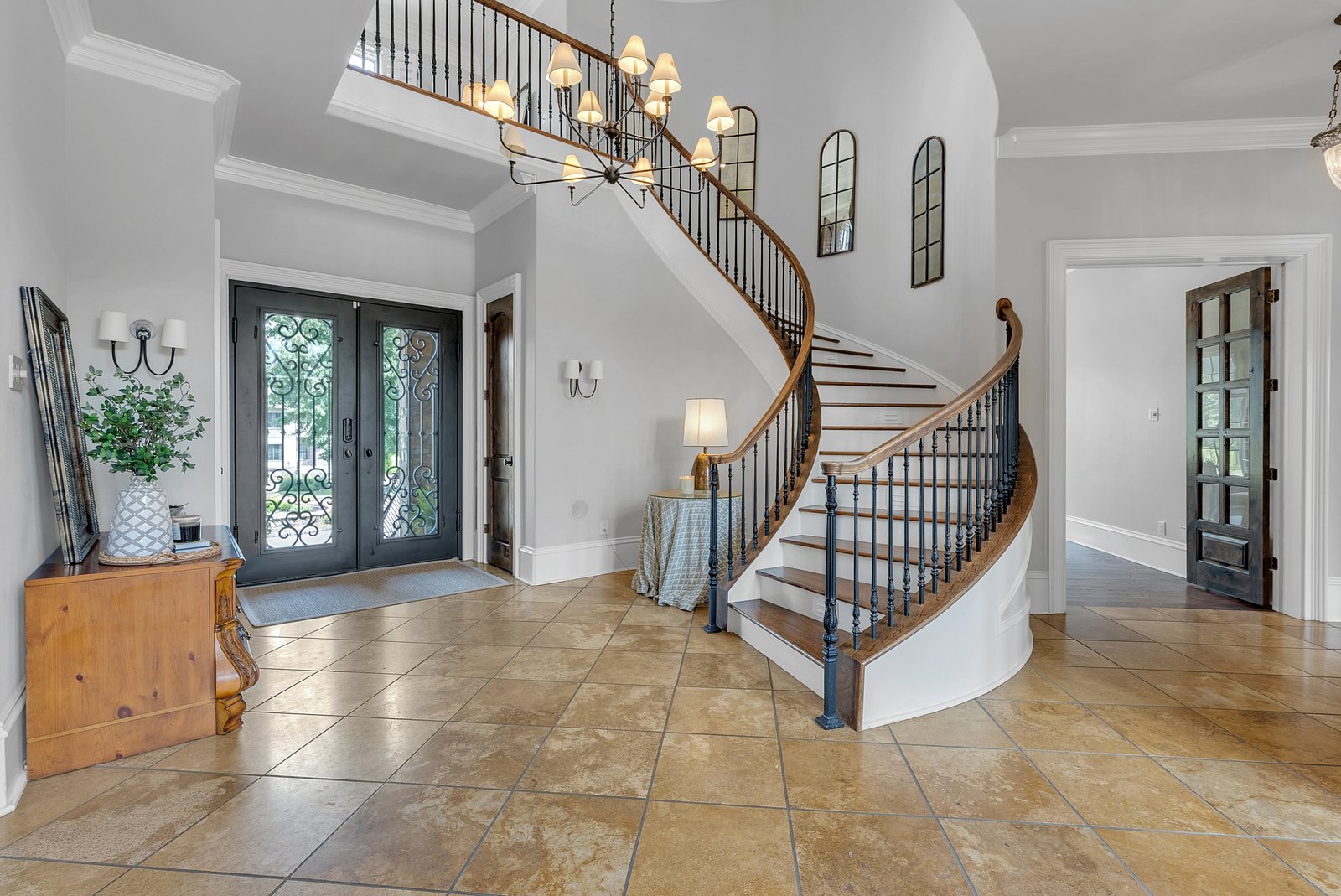 An entry hall with a curved staircase and iron front doors