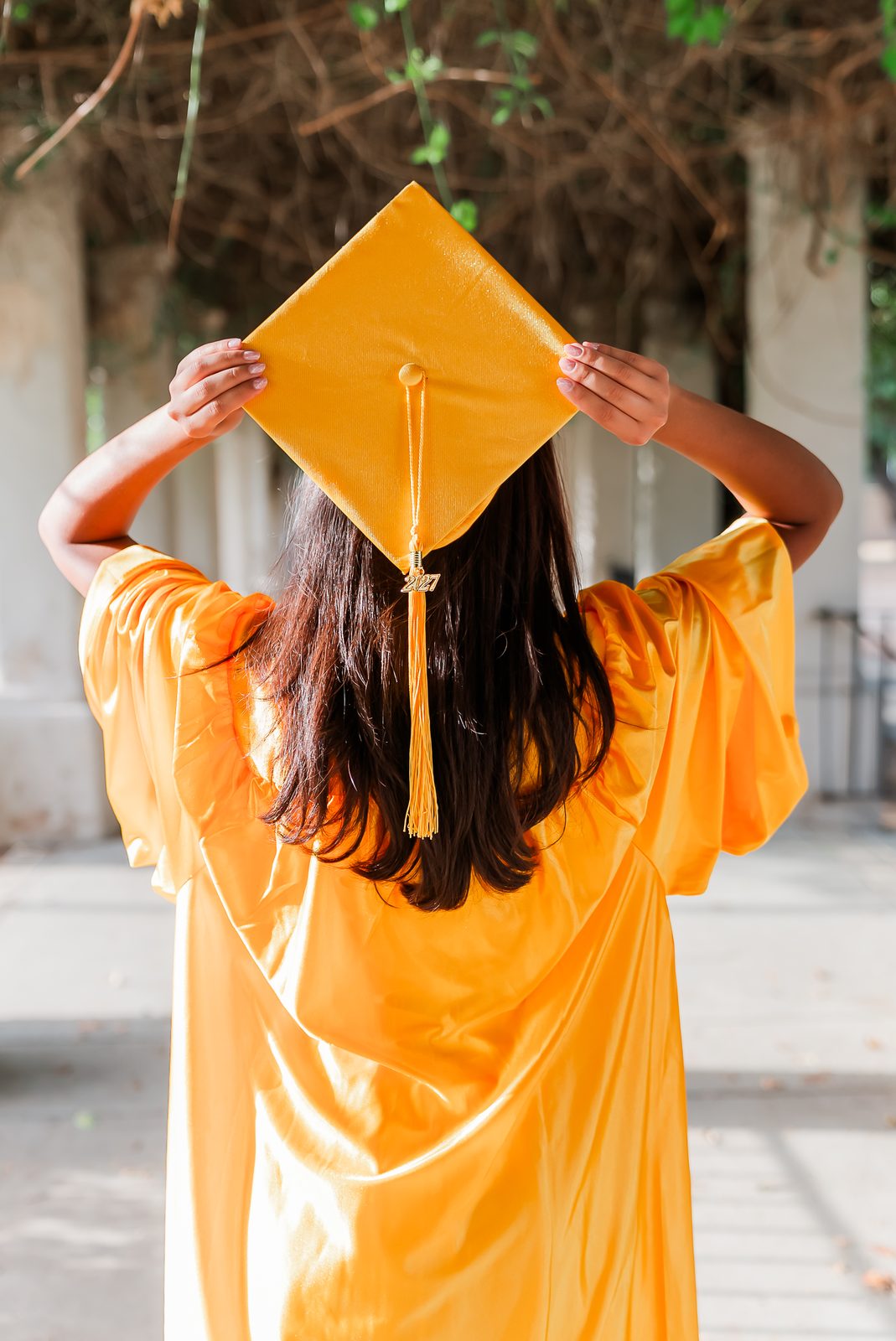 A graduate photographed from behind holding her cap above her head