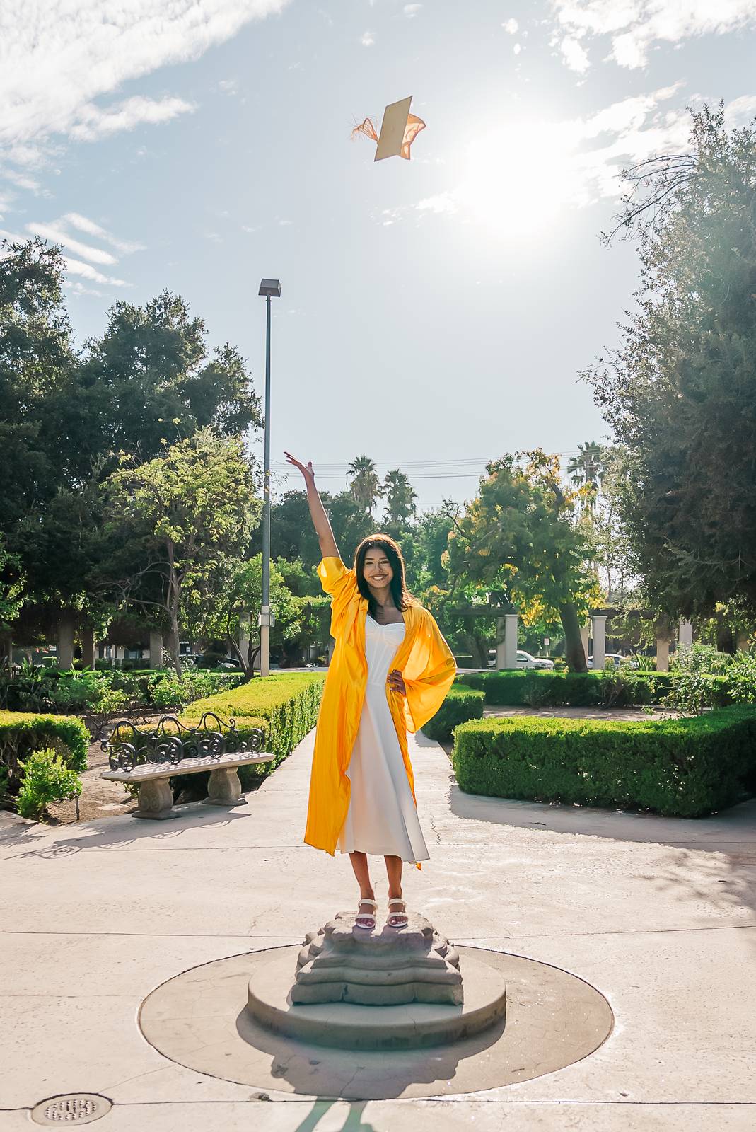 A graduate tossing her cap while standing on a garden pedestal