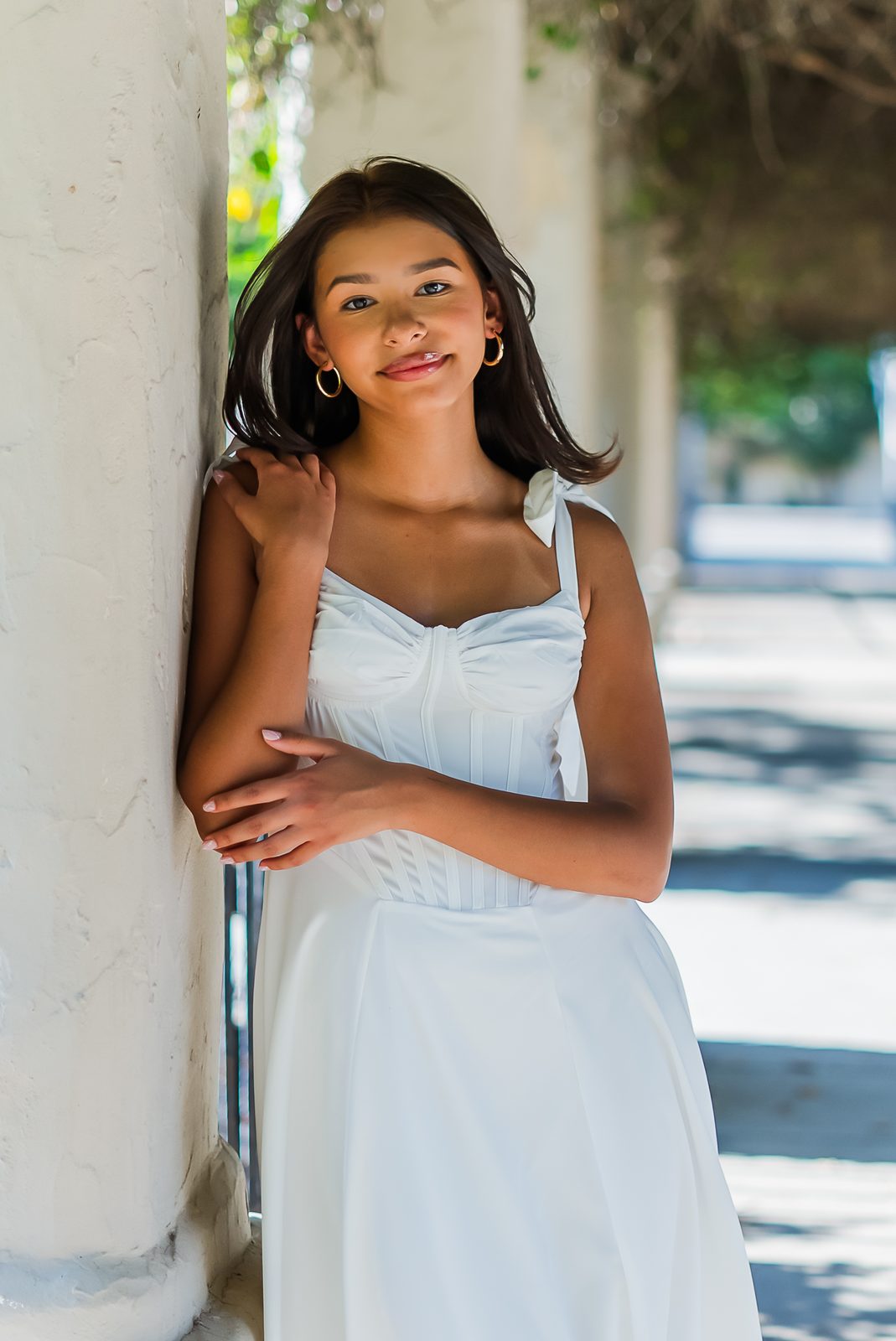 A high school senior in a white dress leaning against a column
