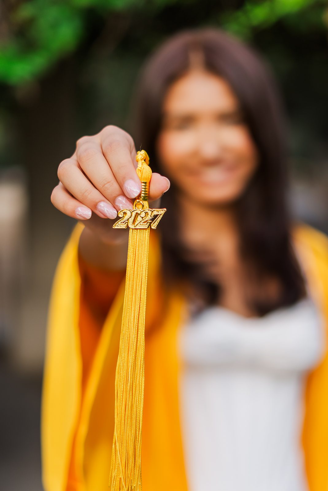 A class of 2027 tassel held toward camera, the graduate soft behind it