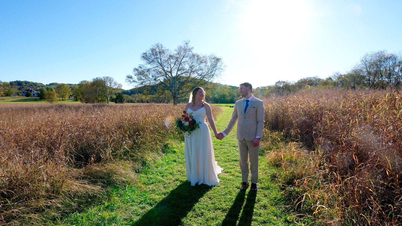 A couple holding hands in a tall autumn field under a clear sky