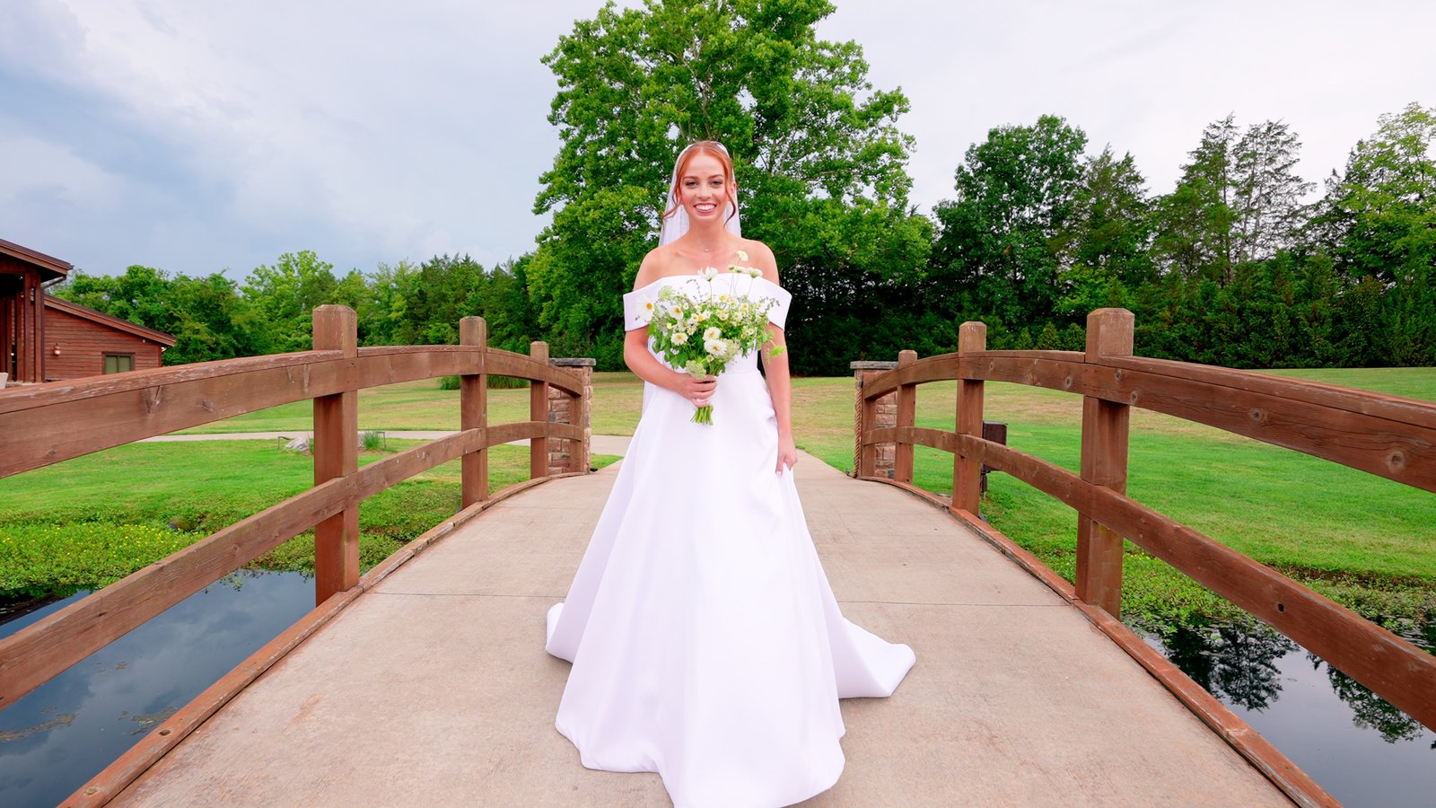 A bride walking across a wooden bridge holding a bouquet of daisies