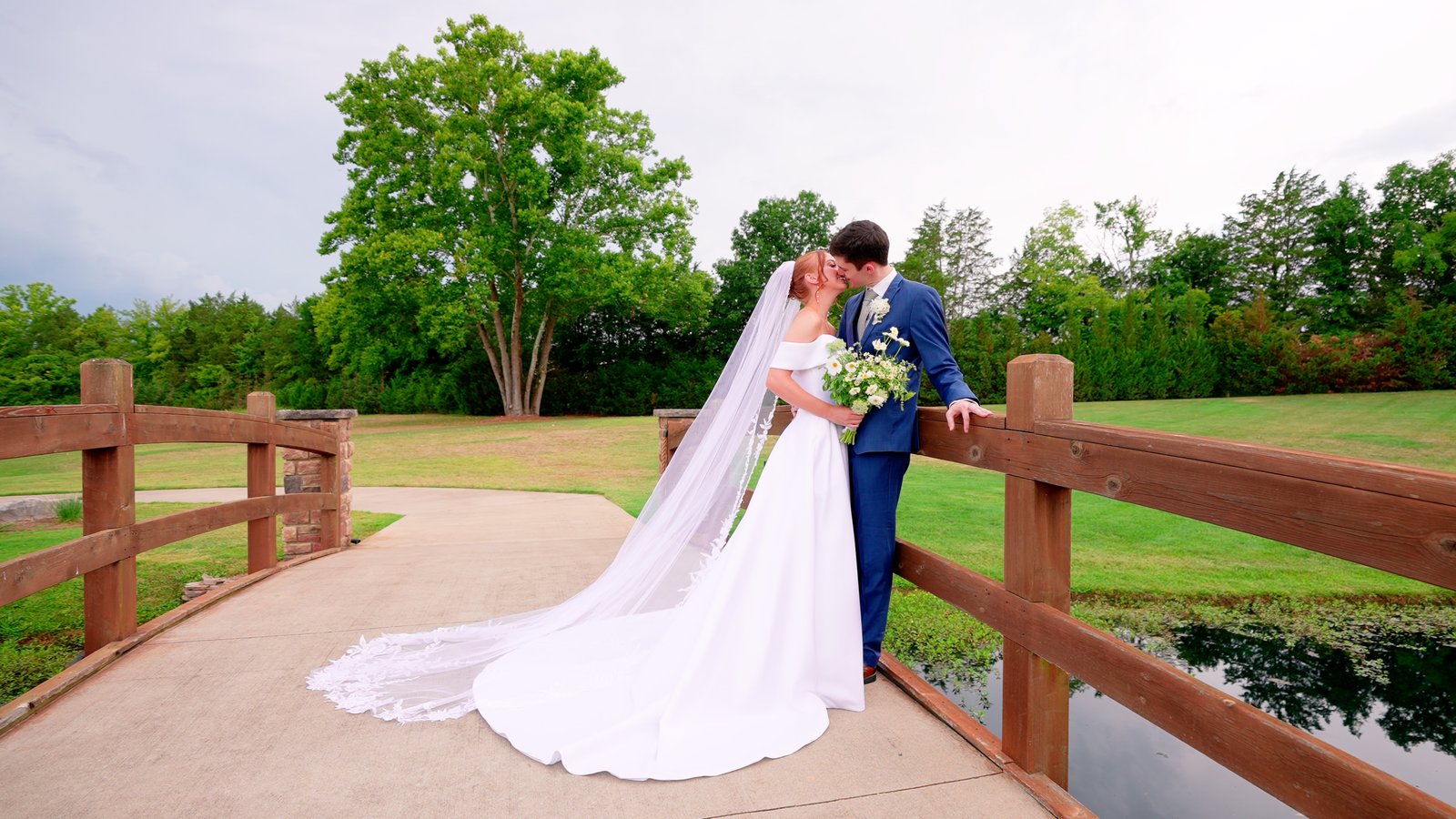 A couple kissing on a bridge, the bride's veil and train spread behind her