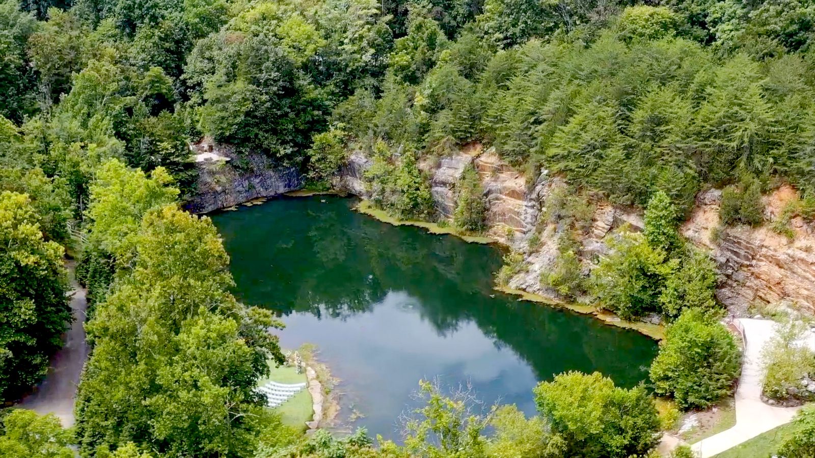 An aerial view of a quarry lake wedding venue, ceremony chairs set on the lawn beside the water