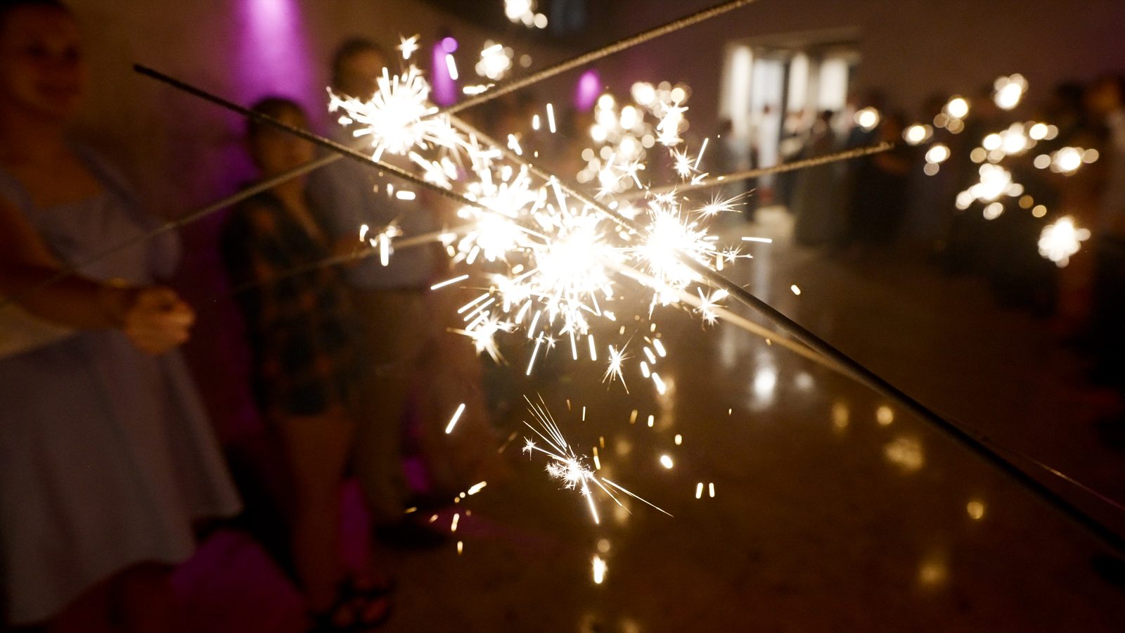 Sparklers crossing during a reception send-off, guests glowing out of focus behind